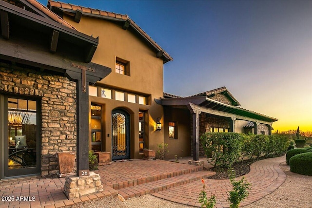 view of exterior entry with a tile roof, stone siding, and stucco siding