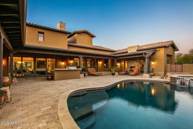 pool at dusk featuring a pool with connected hot tub, outdoor dry bar, and a patio area