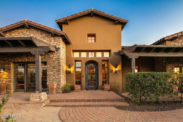 property entrance featuring a tile roof, stone siding, and stucco siding