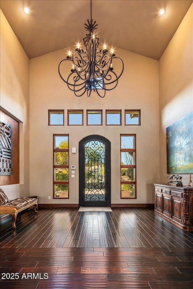 foyer with a notable chandelier, baseboards, wood-type flooring, and high vaulted ceiling