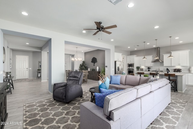 living room featuring ceiling fan with notable chandelier and light hardwood / wood-style flooring