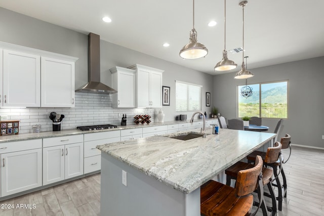 kitchen with an island with sink, wall chimney exhaust hood, and white cabinets