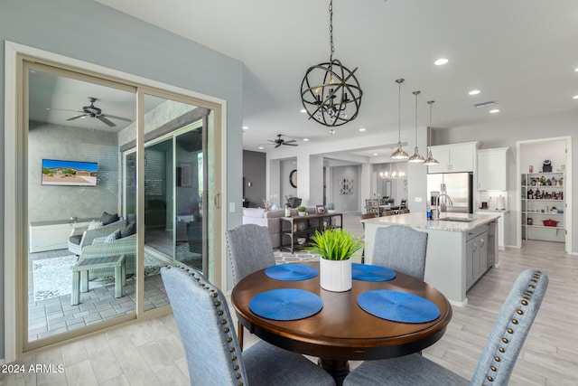 dining space with light wood-type flooring, sink, and ceiling fan with notable chandelier