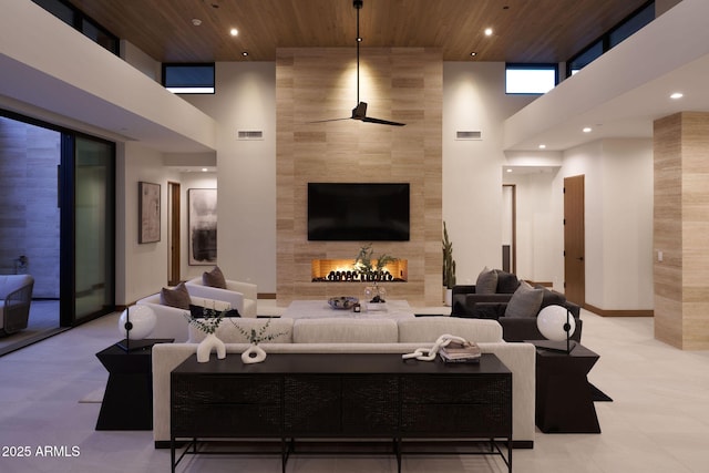 living room featuring ceiling fan, wood ceiling, a tiled fireplace, and a towering ceiling