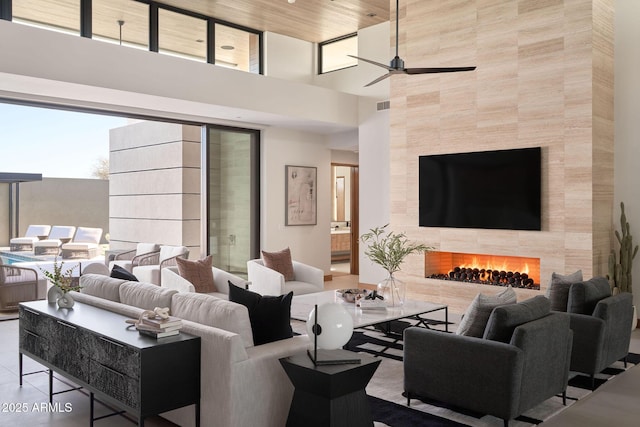 tiled living room with ceiling fan, a towering ceiling, and a fireplace