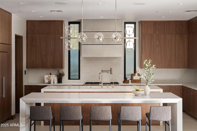 kitchen featuring sink, a breakfast bar, backsplash, and a kitchen island with sink