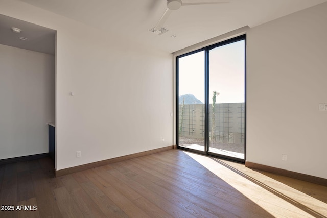 spare room featuring ceiling fan, expansive windows, and hardwood / wood-style flooring