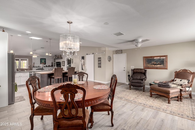 dining space featuring light wood finished floors, a barn door, visible vents, lofted ceiling, and ceiling fan