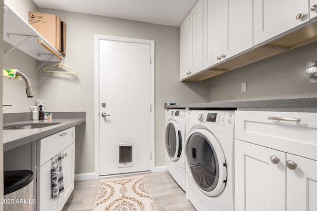 clothes washing area featuring washer and clothes dryer, cabinet space, a sink, light wood-type flooring, and baseboards