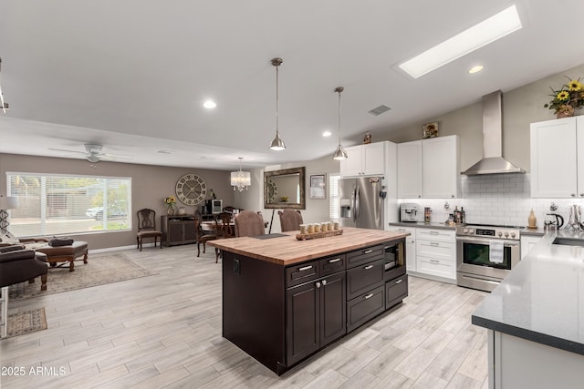 kitchen featuring stainless steel appliances, open floor plan, white cabinetry, and wall chimney range hood