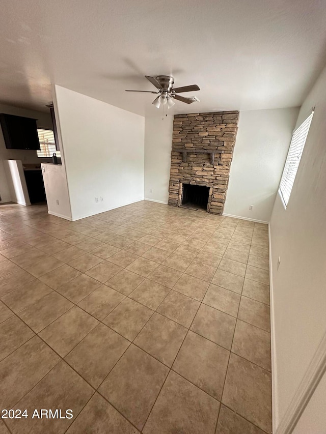 unfurnished living room with light tile patterned flooring, a stone fireplace, and ceiling fan