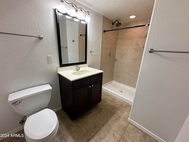 bathroom featuring vanity, toilet, a tile shower, and tile patterned flooring