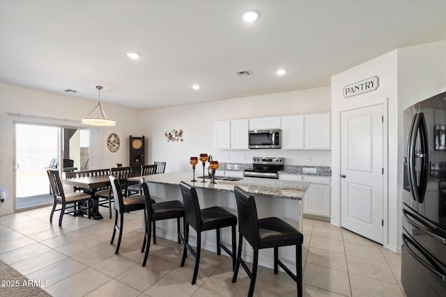 kitchen featuring white cabinetry, appliances with stainless steel finishes, light stone countertops, and an island with sink