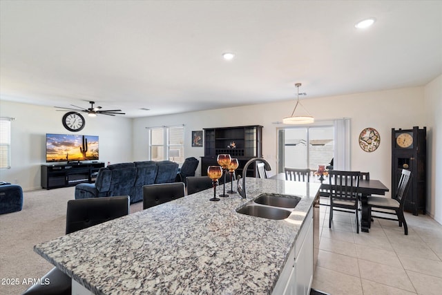 kitchen with pendant lighting, sink, white cabinetry, a kitchen island with sink, and light stone counters