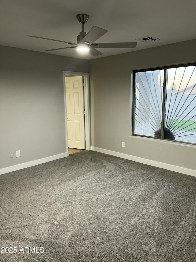 unfurnished room featuring baseboards, visible vents, dark colored carpet, and ceiling fan