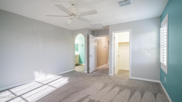 unfurnished bedroom with a walk in closet, ensuite bathroom, light colored carpet, ceiling fan, and a closet