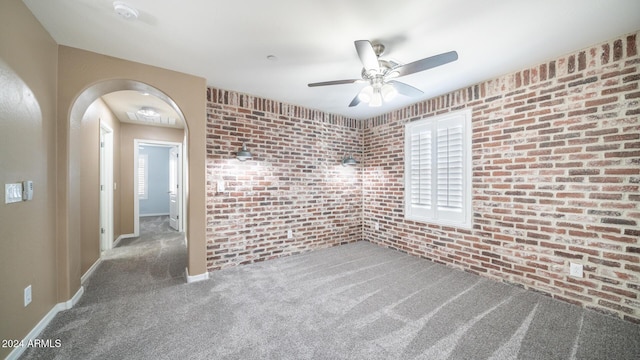 unfurnished room with carpet flooring, ceiling fan, and brick wall