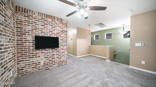 unfurnished living room featuring carpet flooring, ceiling fan, and brick wall