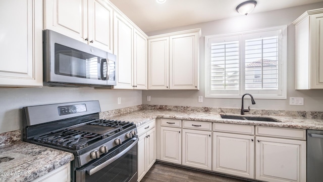 kitchen with light stone countertops, appliances with stainless steel finishes, dark wood-type flooring, sink, and white cabinetry