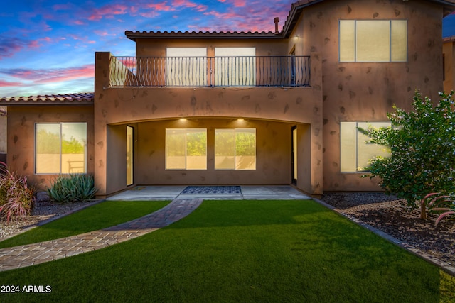 back house at dusk with a balcony, a yard, and a patio area