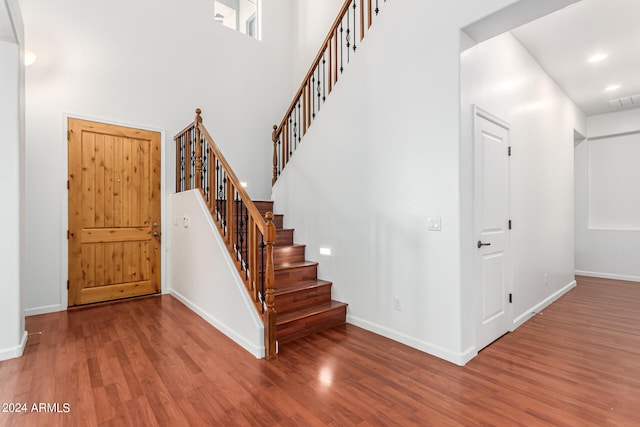 entryway with wood-type flooring and a towering ceiling