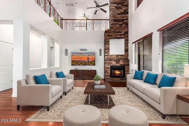 living room featuring ceiling fan, a stone fireplace, wood-type flooring, and a high ceiling