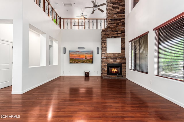 unfurnished living room featuring a high ceiling, a fireplace, dark hardwood / wood-style floors, and ceiling fan