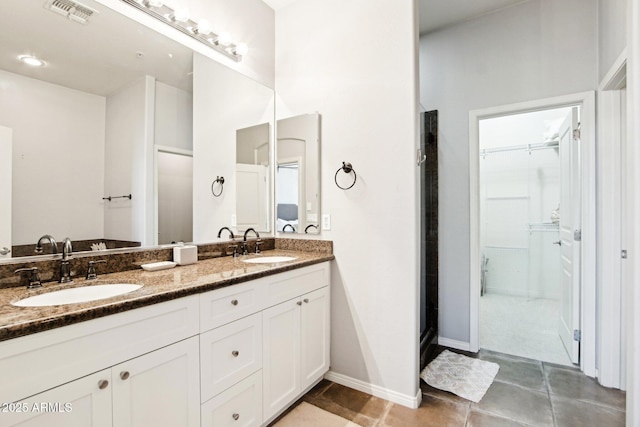 bathroom with a walk in closet, double vanity, tile patterned floors, and baseboards