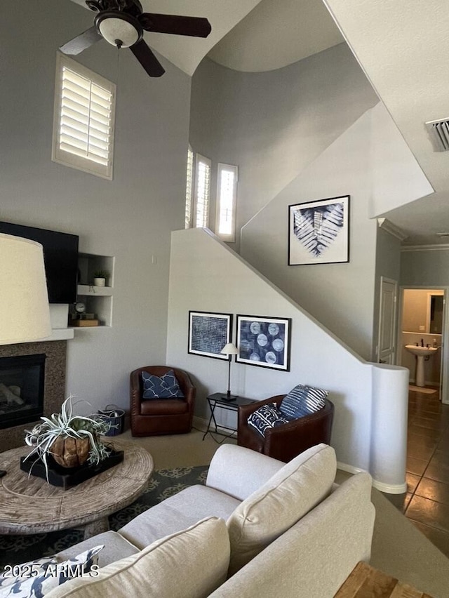 living area with ceiling fan, a high ceiling, tile patterned floors, a glass covered fireplace, and crown molding