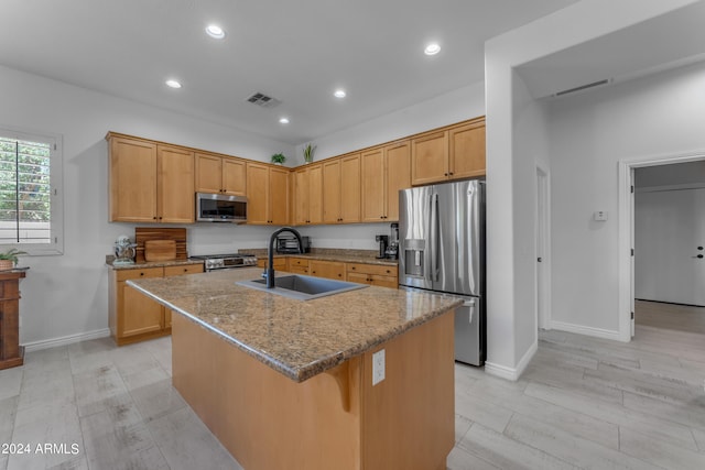 kitchen with light stone counters, stainless steel appliances, light hardwood / wood-style flooring, a kitchen island with sink, and sink