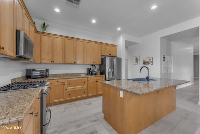 kitchen featuring light stone counters, an island with sink, appliances with stainless steel finishes, and sink