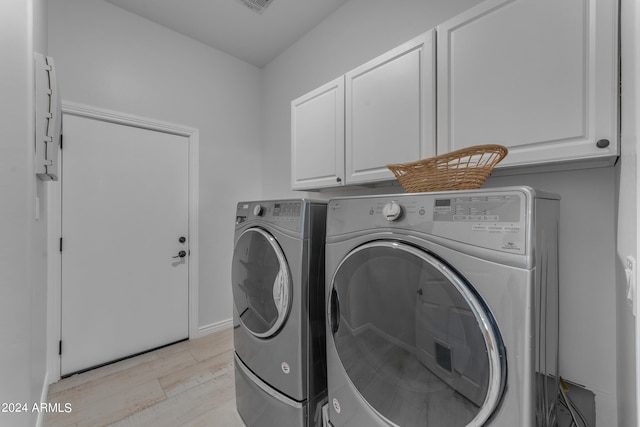 laundry room featuring washer and clothes dryer, cabinets, and light hardwood / wood-style flooring