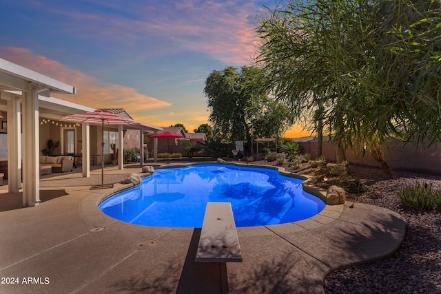 pool at dusk with an outdoor living space, a patio area, and a diving board