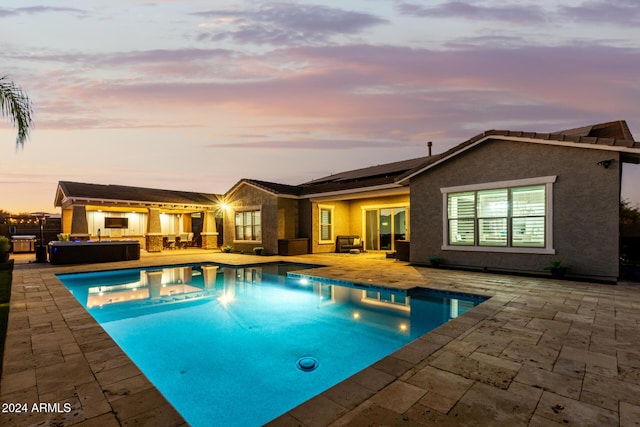 pool at dusk featuring a hot tub and a patio area