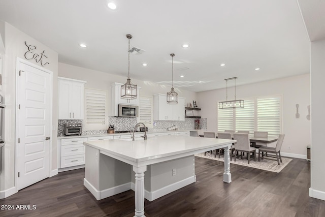 kitchen featuring a kitchen island with sink, dark hardwood / wood-style flooring, decorative light fixtures, a kitchen bar, and white cabinetry