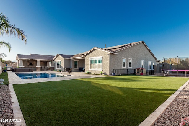 back of house with a lawn, a swimming pool with hot tub, a trampoline, and a patio