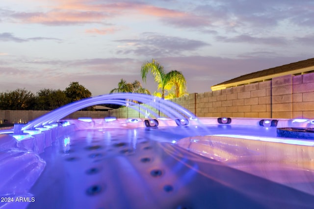 pool at dusk featuring a hot tub