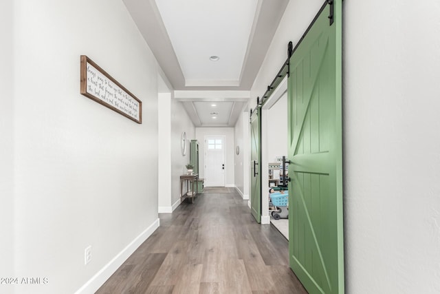 corridor with a raised ceiling, a barn door, and hardwood / wood-style flooring