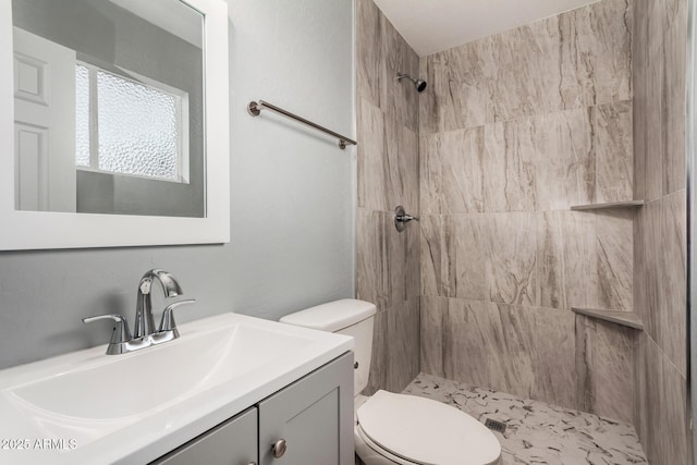 bathroom with tiled shower, vanity, and toilet