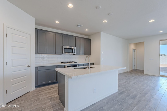 kitchen with a center island with sink, gray cabinetry, stainless steel appliances, decorative backsplash, and sink