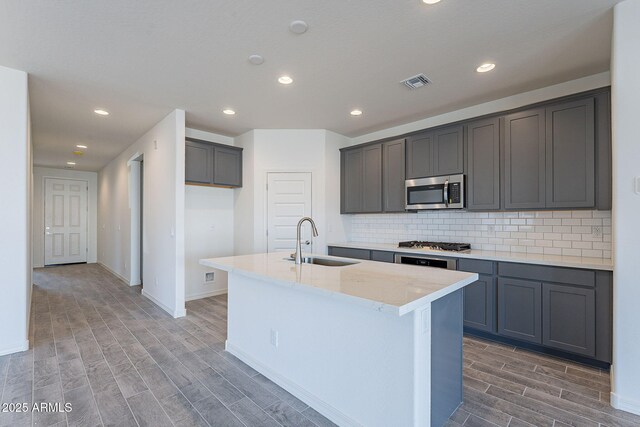 kitchen with an island with sink, appliances with stainless steel finishes, gray cabinets, and sink