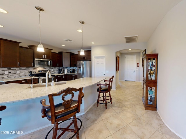 17547 W Gambit Trl, Surprise, AZ 85387 - kitchen with stainless steel appliances, a breakfast bar area, a sink, arched walkways, and decorative backsplash