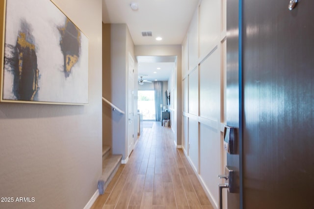 hallway featuring stairs, light wood-type flooring, visible vents, and baseboards