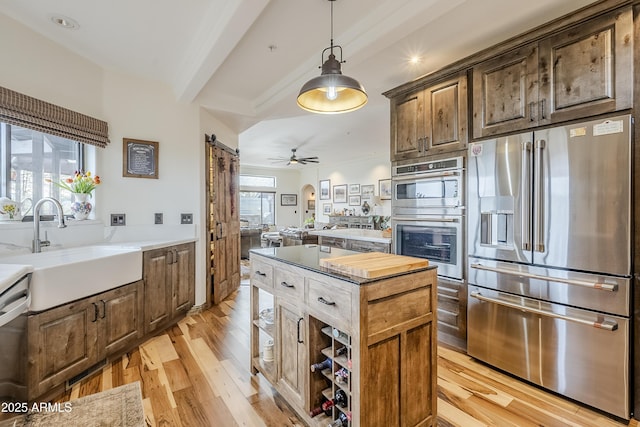 kitchen featuring arched walkways, a barn door, light wood-style flooring, stainless steel appliances, and a sink