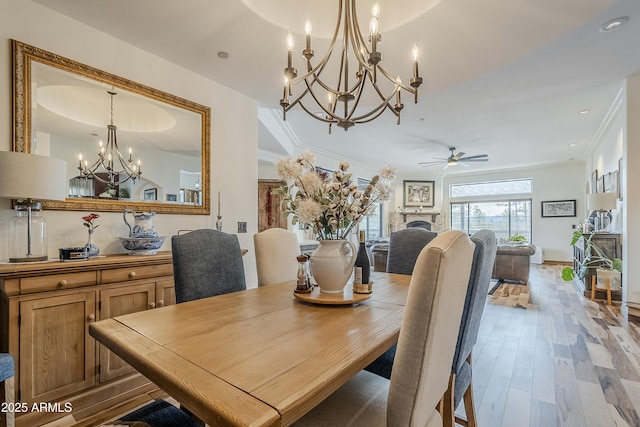 dining space featuring ceiling fan with notable chandelier, a fireplace, baseboards, light wood finished floors, and crown molding