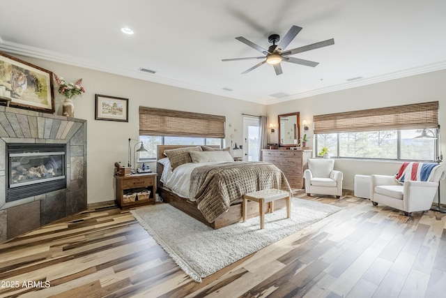 bedroom with ornamental molding, a tiled fireplace, wood finished floors, and visible vents