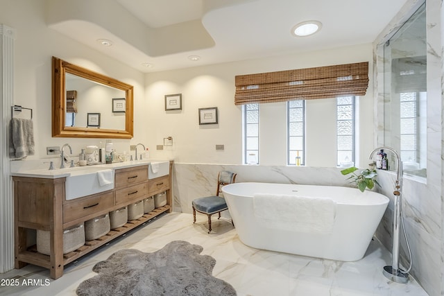 bathroom featuring double vanity, a soaking tub, a sink, marble finish floor, and tile walls