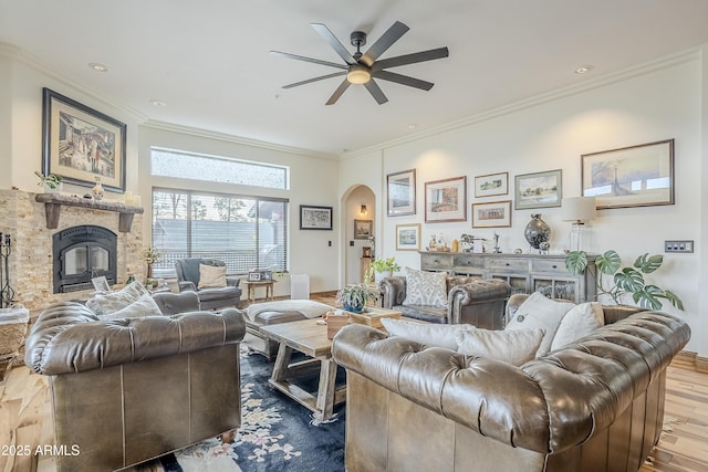 living area featuring ornamental molding, arched walkways, a stone fireplace, and wood finished floors