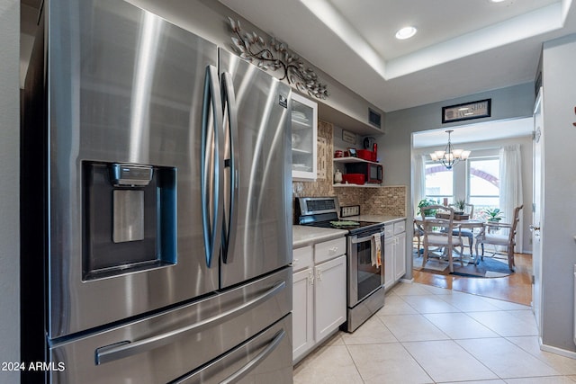 kitchen featuring light tile patterned flooring, white cabinetry, an inviting chandelier, stainless steel appliances, and a raised ceiling