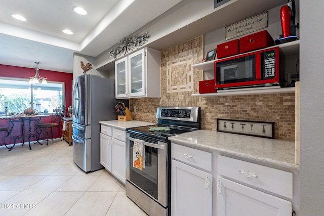 kitchen with tasteful backsplash, white cabinets, appliances with stainless steel finishes, light tile patterned floors, and decorative light fixtures